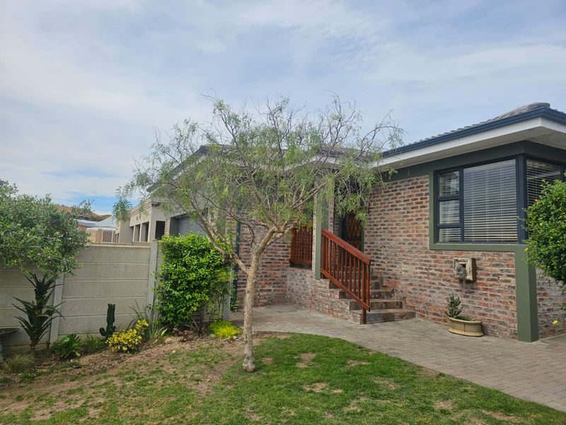 A well-maintained rear exterior view featuring a brick facade, paved patio area, and timber staircase leading to the entrance.