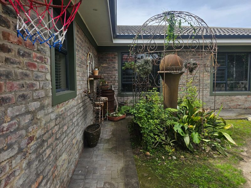 A rear exterior view of the house featuring brick walls, a paved walkway, and a landscaped garden area with a decorative metal structure.