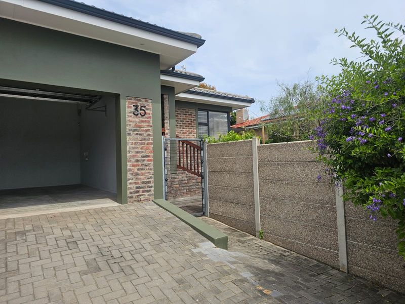Front exterior view of the property featuring a paved driveway, integrated garage, brick facade detailing, and a secure pedestrian gate with boundary walling.