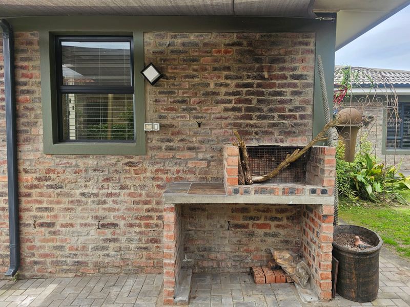Outdoor patio area featuring a built-in brick braai, paved flooring, and an exterior wall with a window.