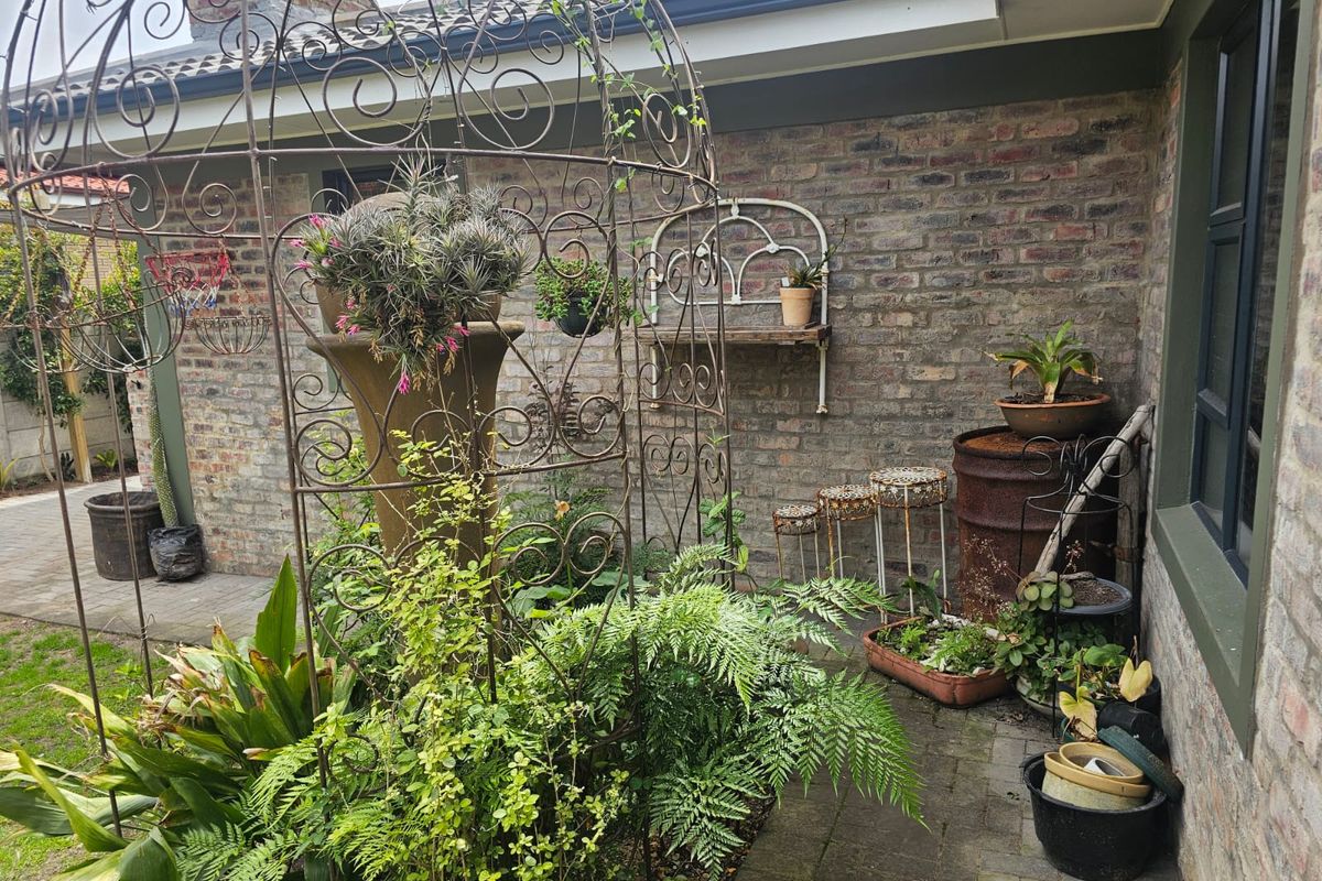 A private garden corner featuring exposed brick walls, paved flooring, and a covered roof section, creating a cozy outdoor space.