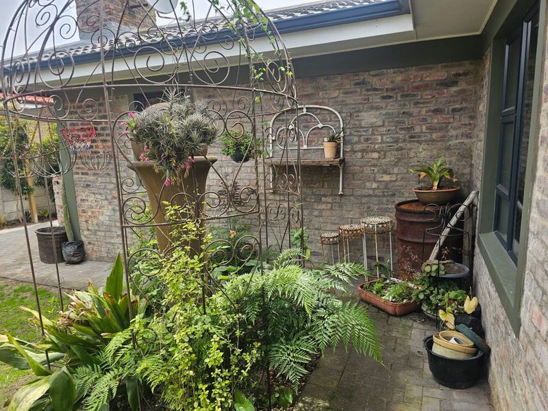 A private garden corner featuring exposed brick walls, paved flooring, and a covered roof section, creating a cozy outdoor space.