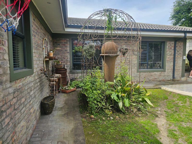 A rear exterior view of the house featuring face brick walls, dark aluminium window frames, and a paved patio area adjacent to a garden.