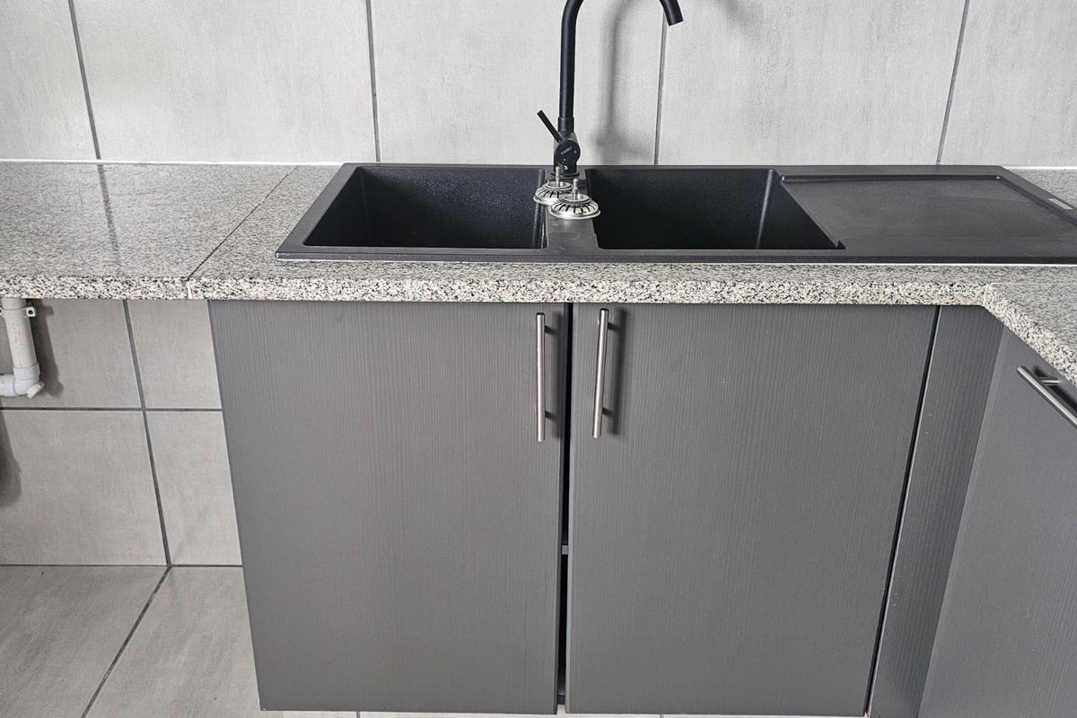 A modern kitchen area featuring grey cabinetry, a granite countertop, and a contemporary black double basin sink with a matching gooseneck faucet.