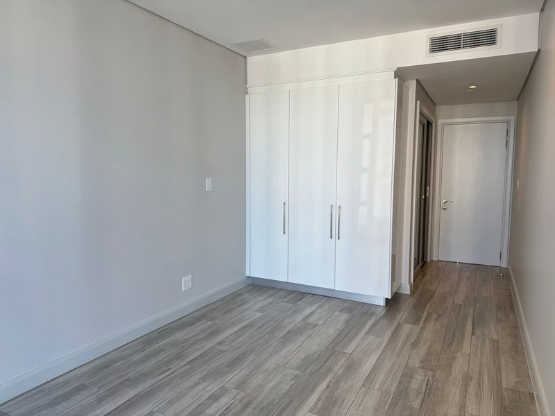 A bright, modern bedroom featuring sleek built-in cupboards, neutral walls, and high-quality laminate flooring with integrated ducted air conditioning.