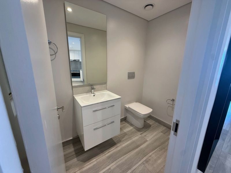 A modern, minimalist guest bathroom featuring a wall-mounted vanity with integrated basin, wall-mounted toilet, and sleek wood-look tiled flooring.