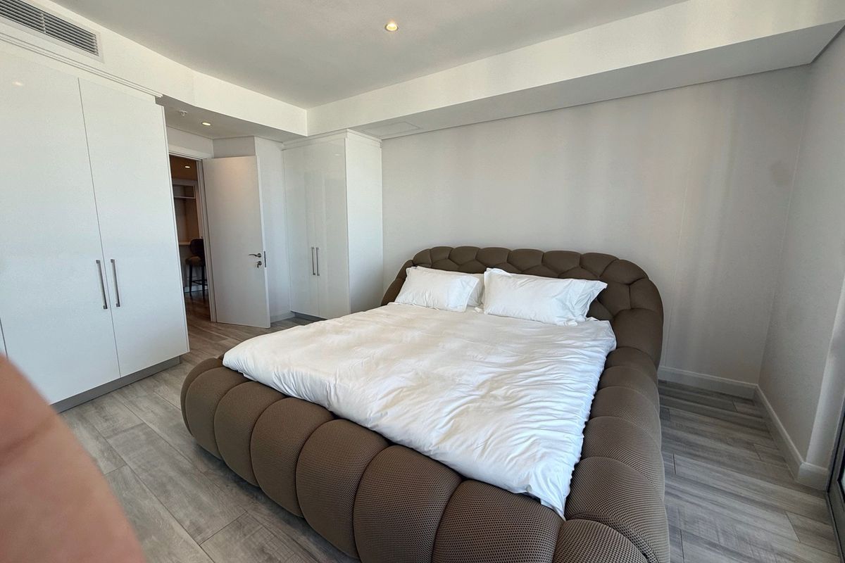 Modern bedroom featuring light wood-look laminate flooring, built-in white wardrobes, and integrated ducted air conditioning.