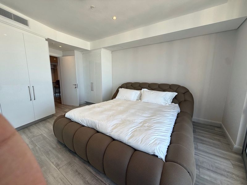 Modern bedroom featuring light wood-look laminate flooring, built-in white wardrobes, and integrated ducted air conditioning.