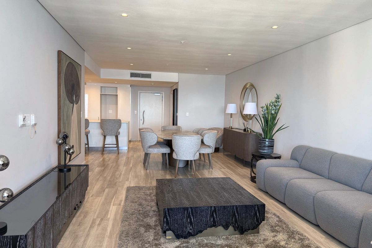 A modern open-plan living and dining area featuring wood-look tile flooring, recessed lighting, and a seamless transition to the kitchen breakfast bar.