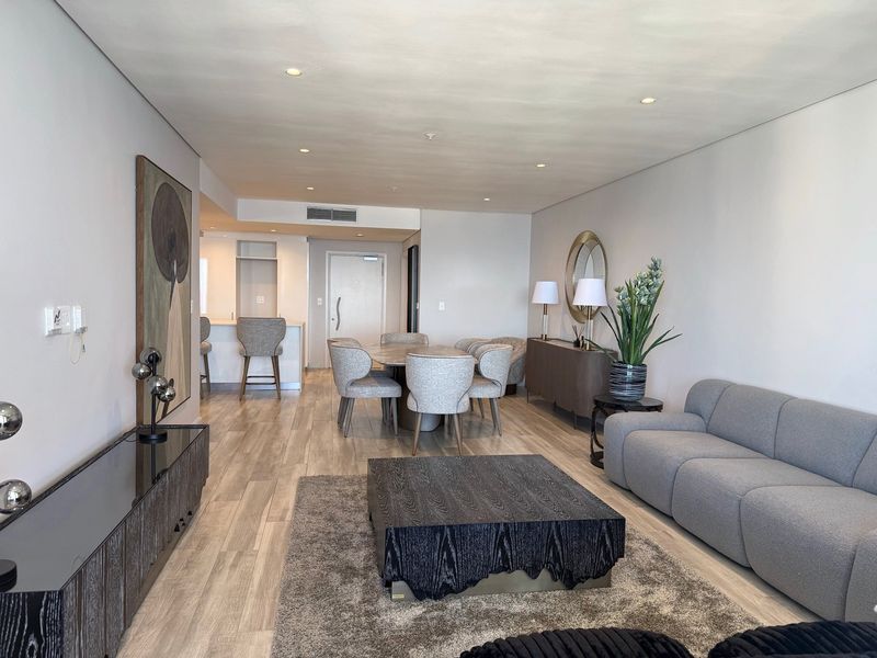 A modern open-plan living and dining area featuring wood-look tile flooring, recessed lighting, and a seamless transition to the kitchen breakfast bar.