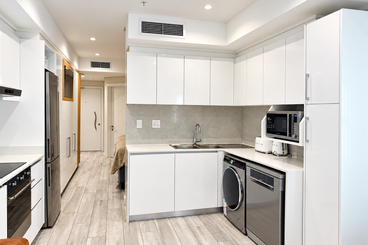 Modern, high-gloss white kitchen featuring integrated appliances, stone countertops, and sleek cabinetry, seamlessly flowing into the apartment hallway.