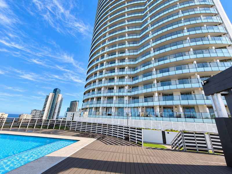 Modern apartment complex featuring a swimming pool with composite decking, glass balustrades, and expansive views of the surrounding high-rise architecture.