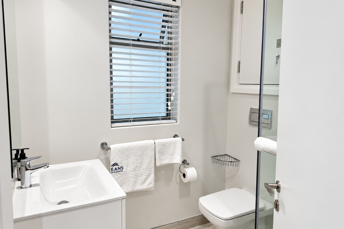 A modern, well-maintained bathroom featuring a wall-mounted toilet, vanity basin with mixer tap, and a glass shower screen with neutral tiled flooring.