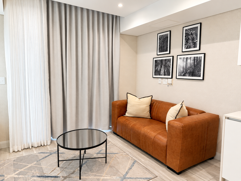 A modern, well-maintained living area featuring neutral wall finishes, tiled flooring, recessed ceiling lighting, and floor-to-ceiling curtains providing access to natural light.