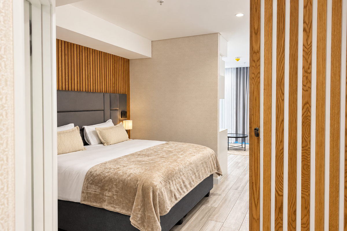 A modern bedroom featuring elegant timber slat wall paneling, wood-look tile flooring, and recessed ceiling lighting, creating a warm and sophisticated atmosphere.