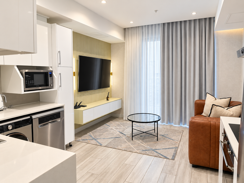 Modern open-plan living area featuring a sleek kitchen with integrated appliances, slatted feature wall, floating media console, and neutral tiled flooring.