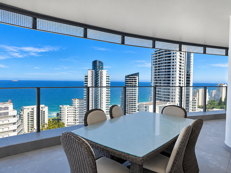 Spacious covered balcony featuring modern tiled flooring, a sleek glass balustrade, and panoramic ocean and city skyline views.
