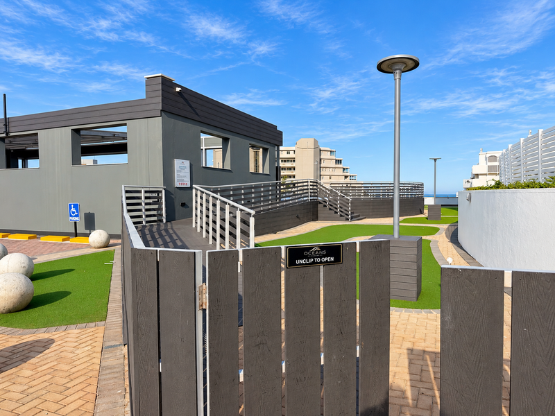 A modern, well-maintained outdoor terrace area featuring timber decking, ramp access, and landscaped artificial lawn sections, providing a clean and accessible communal space.