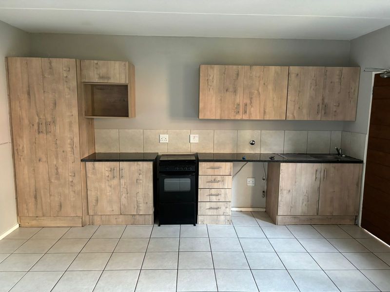 A clean, functional kitchen featuring light wood-look cabinetry, dark countertops, tiled backsplash, and a freestanding stove, offering a neutral space ready for personalization.