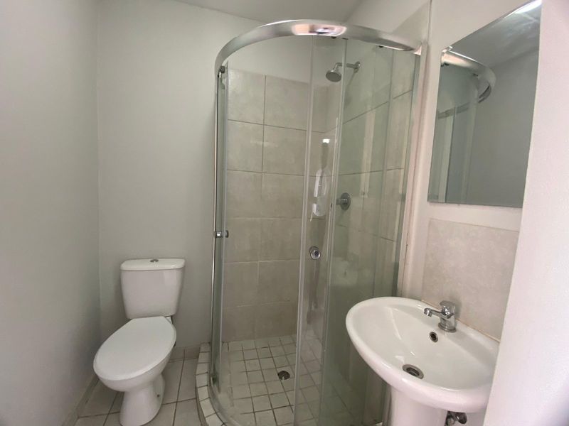 A functional bathroom featuring a curved glass shower enclosure, pedestal basin, and toilet with neutral wall tiling.