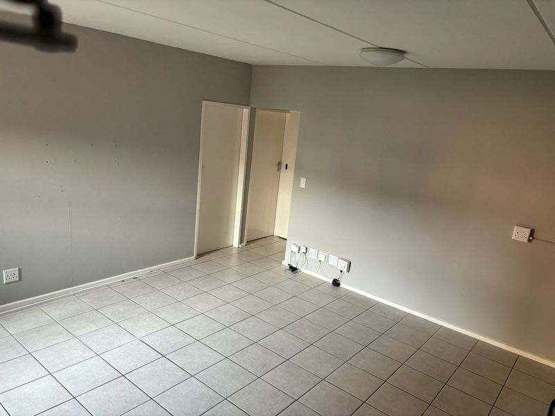 An empty living area featuring neutral grey walls, tiled flooring, and multiple electrical points, providing a blank canvas for interior design.