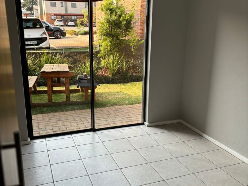 An empty living area featuring neutral ceramic floor tiles and a large sliding glass door providing direct access to a private patio and garden.