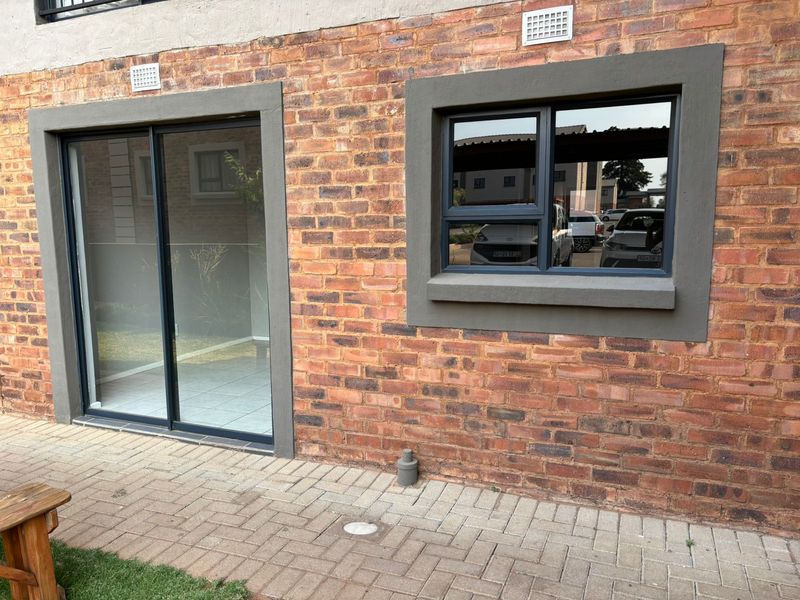Rear exterior view of the apartment featuring a face brick facade, paved patio area, and modern aluminium-framed sliding door and window.