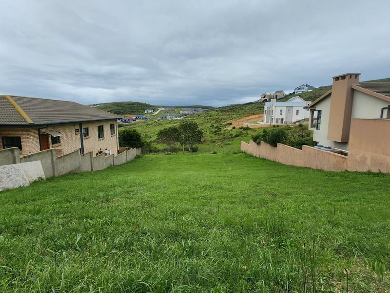 A vacant residential plot of land situated between existing neighboring properties, featuring a grass lawn and established boundary walls.