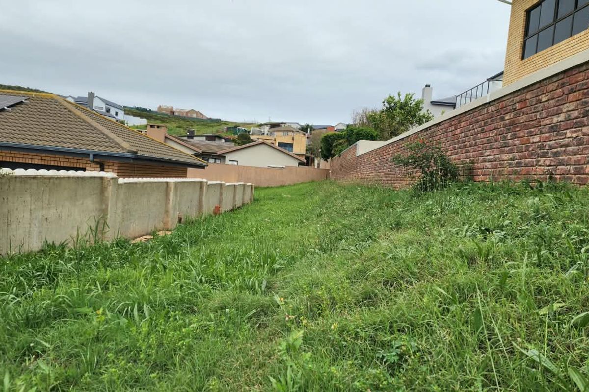 A view of a vacant residential plot featuring established brick and concrete boundary walls, surrounded by neighboring residential properties.