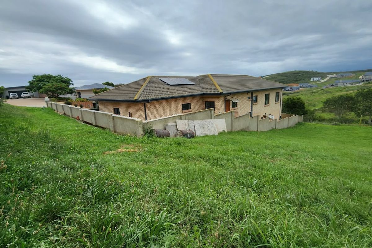 Rear view of a residential property featuring a brick facade, tiled roof with solar panels, and a concrete boundary wall overlooking a grassy slope.