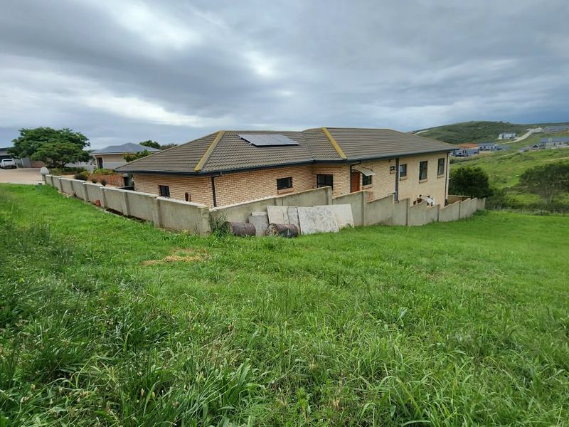 Rear view of a residential property featuring a brick facade, tiled roof with solar panels, and a concrete boundary wall overlooking a grassy slope.