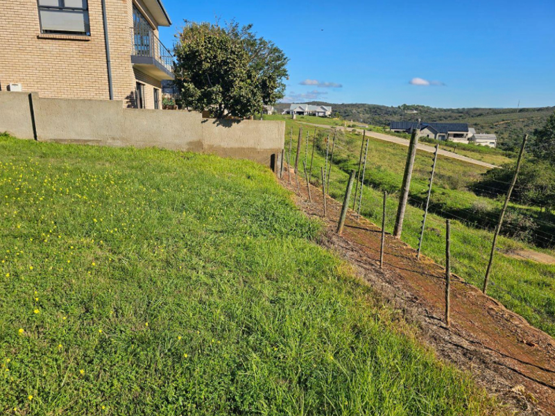 Rear view of the property showing a grassy yard, brick building facade, retaining wall, and electric perimeter fencing overlooking the surrounding landscape.