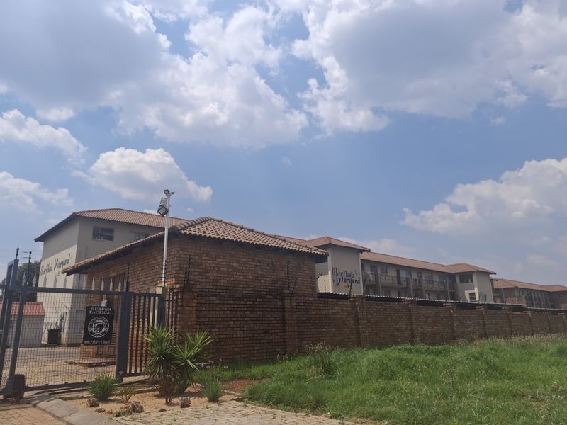 Exterior view of the apartment complex entrance featuring a brick perimeter wall, security gate, and electric fencing.