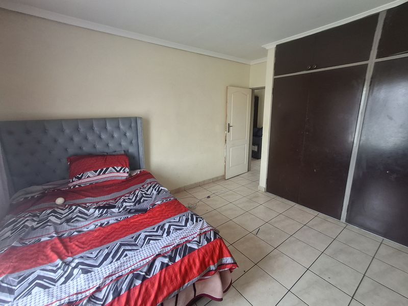 A bedroom featuring tiled flooring and dark built-in cupboards, offering a functional space with potential for cosmetic updates.