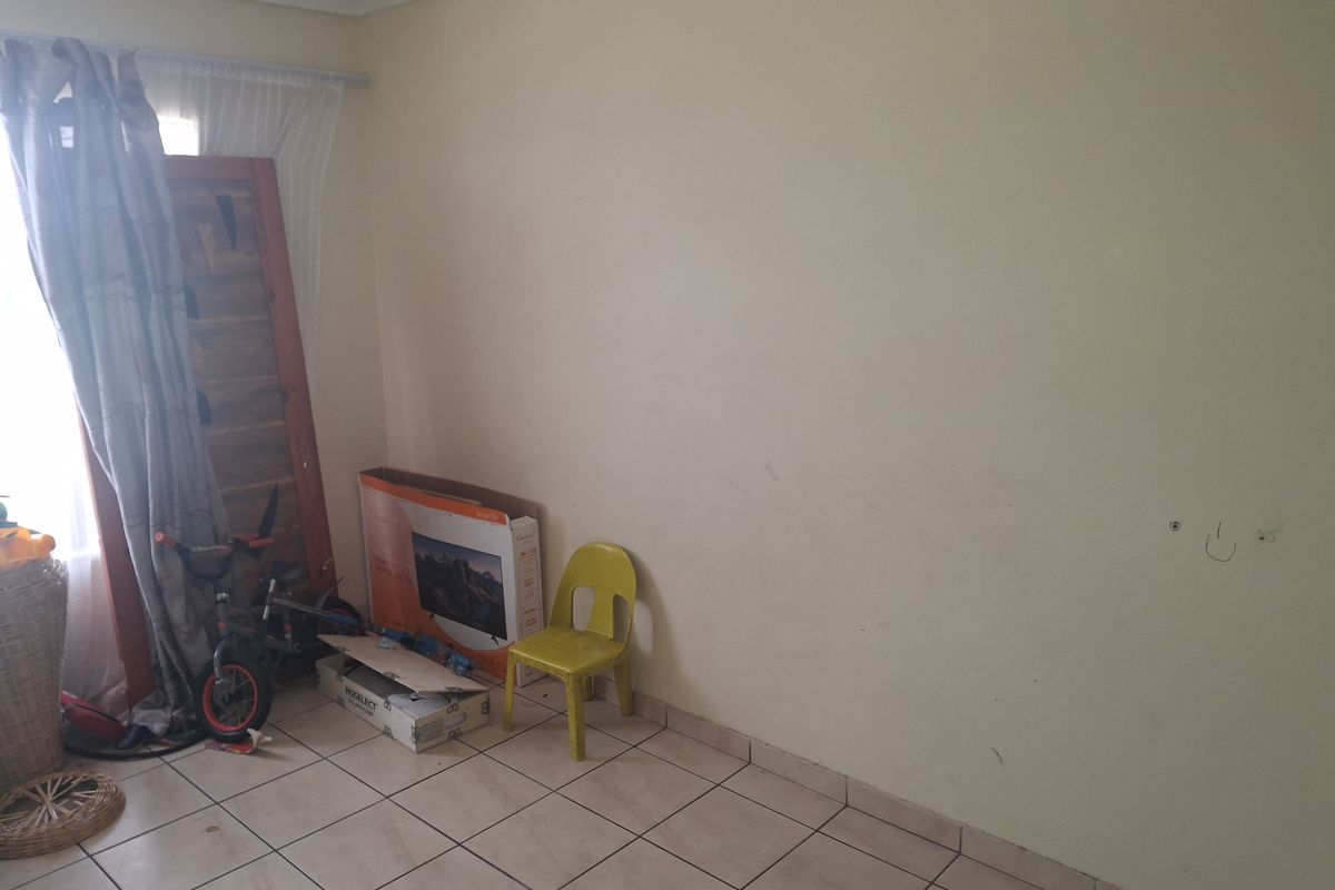 A sparsely furnished living area featuring tiled flooring and neutral walls, offering a blank canvas for potential interior design updates.