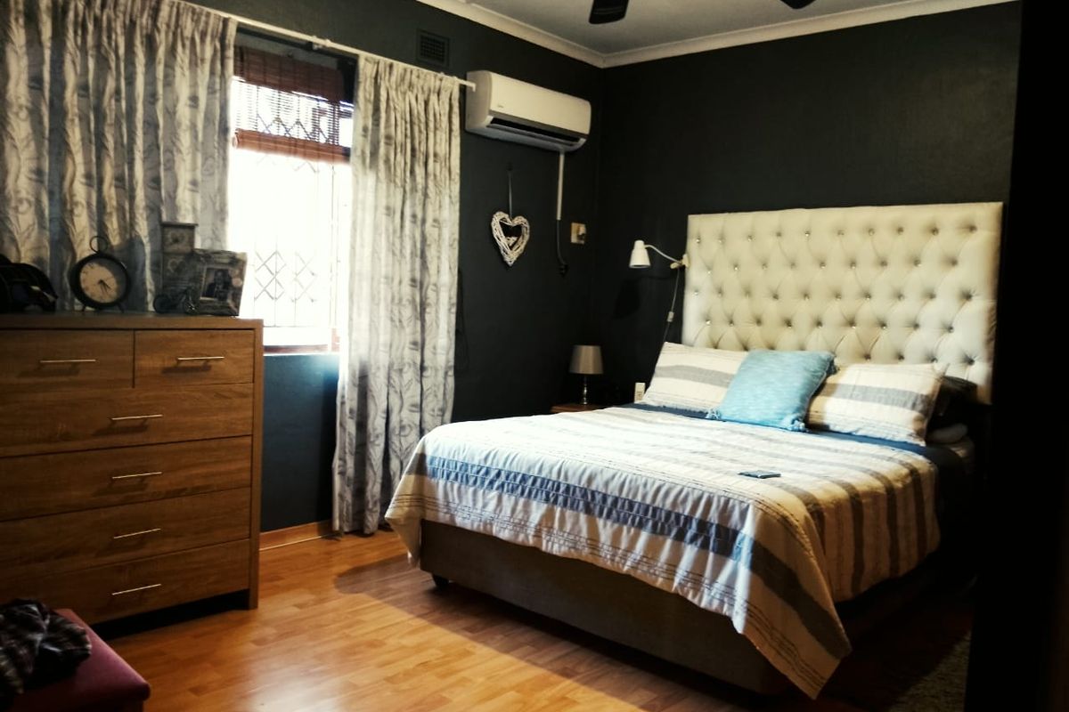 A well-maintained bedroom featuring dark painted walls, laminate flooring, a ceiling fan, and a wall-mounted air conditioning unit.