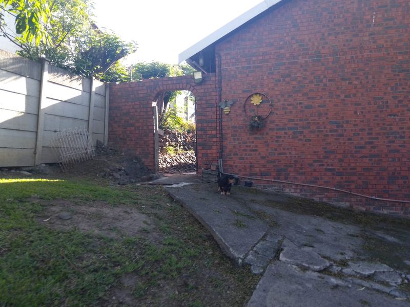Rear exterior view showing a red brick wall, arched gateway, and a concrete pathway leading to the garden area.