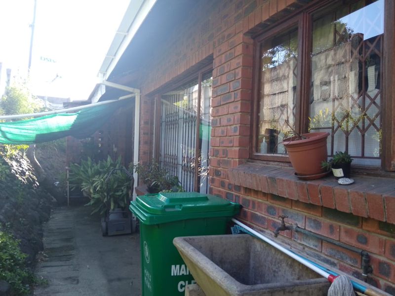 Rear exterior view of the property featuring a brick facade, security gates, timber window frames, and an external concrete wash trough.