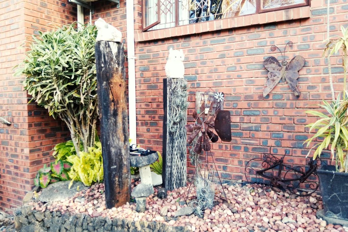 A view of a face brick exterior wall featuring a stone retaining wall, pebble garden bed, and an external air conditioning unit.