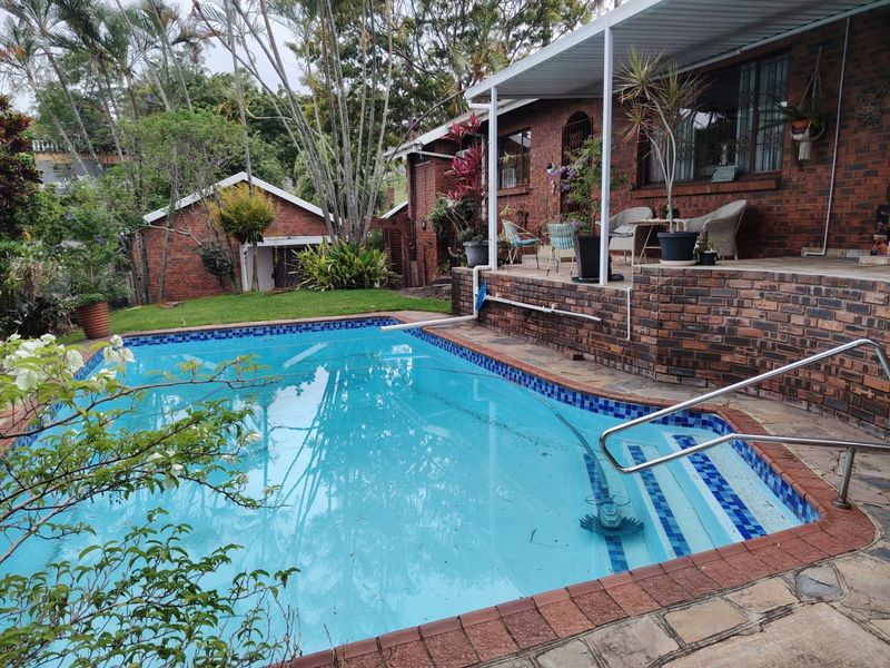 Outdoor pool area featuring a swimming pool with steps, a brick-paved patio, and a covered veranda attached to the main brick house.