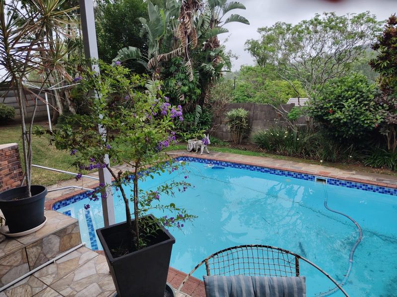 Outdoor pool area featuring a swimming pool with tiled surround and brick boundary wall, set within a landscaped garden.