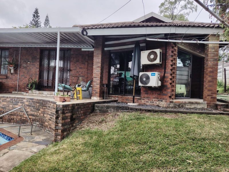 Rear view of a face brick house featuring a covered patio, swimming pool, and integrated air conditioning units.