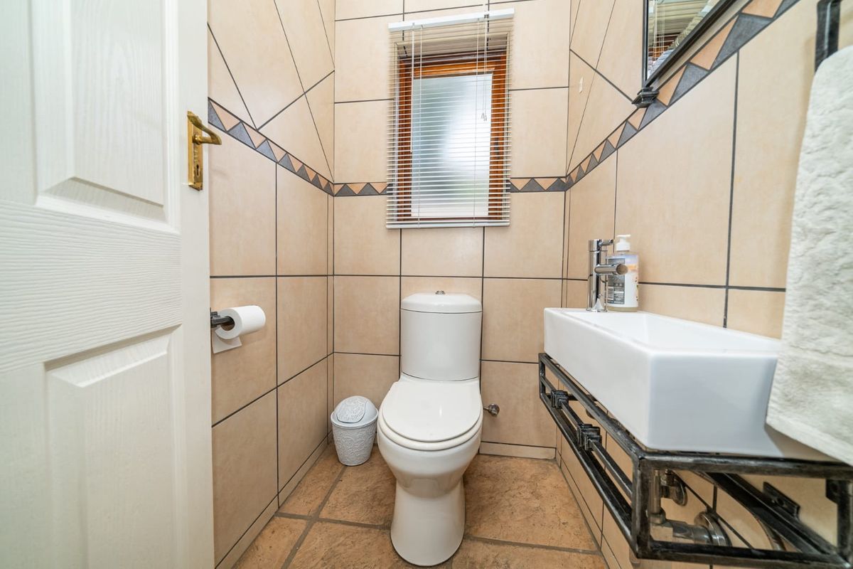 A compact guest bathroom featuring tiled walls and flooring, a modern wall-mounted basin, and a standard toilet.