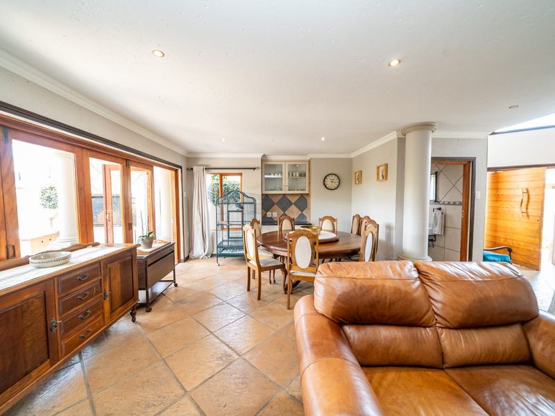 Spacious open-plan living and dining area featuring terracotta floor tiles, recessed lighting, and large wooden folding doors leading to the outdoor space.