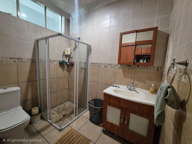 A functional bathroom featuring a shower enclosure, vanity cabinet with integrated sink, medicine cabinet, and neutral ceramic wall and floor tiling.