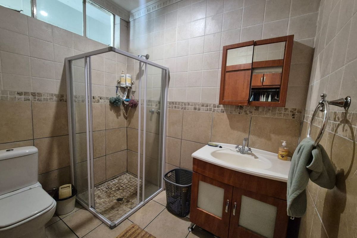 A functional bathroom featuring a shower enclosure, vanity cabinet with integrated sink, medicine cabinet, and neutral ceramic wall and floor tiling.