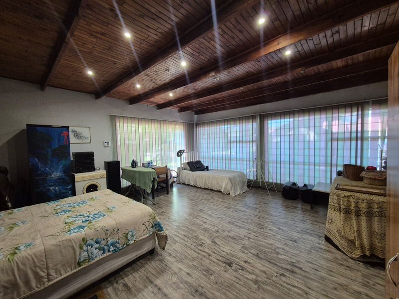 Spacious bedroom featuring exposed timber beam ceilings, recessed lighting, and large windows with vertical blinds, offering a bright and open living space.