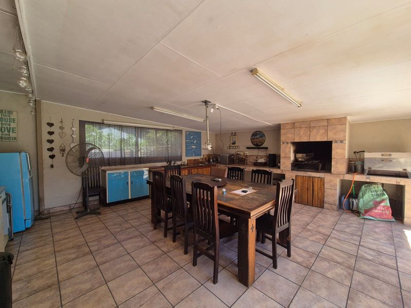 Covered outdoor entertainment area featuring a built-in braai, tiled flooring, and integrated cabinetry, providing a functional space for social gatherings.
