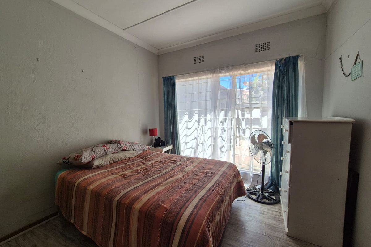 A bedroom featuring laminate flooring, ceiling fan, and ventilation grilles, requiring cosmetic updates to the wall finishes.
