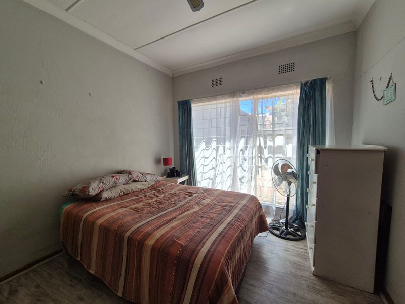 A bedroom featuring laminate flooring, ceiling fan, and ventilation grilles, requiring cosmetic updates to the wall finishes.